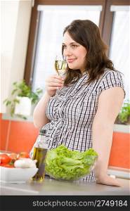 Cook - Plus size happy woman with white wine and lettuce in modern kitchen