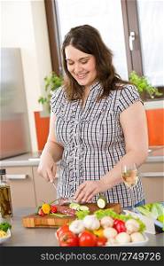 Cook - plus size woman cutting salami and vegetable in modern kitchen