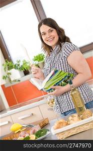 Cook - plus size woman prepare fish with white wine and bread in modern kitchen holding cookbook