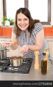 Cook - plus size woman tasting Italian tomato sauce in modern kitchen