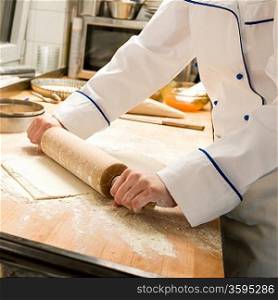 Cook rolling dough in kitchen with rolling pin and flour