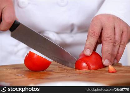 cook slicing tomato on a chopping board