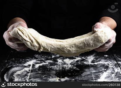 cook stretches kneaded dough from white wheat flour over a black wooden table