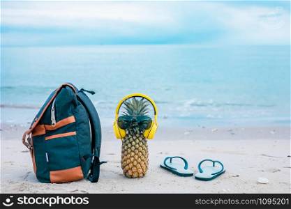 Cook the attractive pineapple in stylish sunglasses, golden bags and headphones in the sand with turquoise water. Tropical summer holiday concept