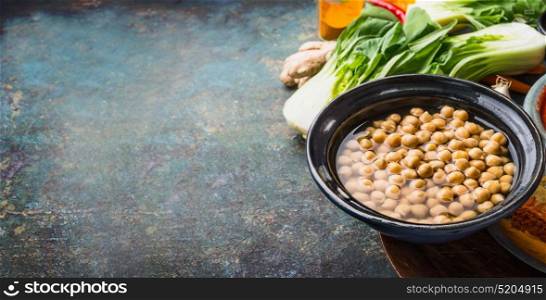 Cooked Chickpeas in bowl with vegetarian cooking ingredients on rustic background, place for text, banner. Healthy food and eating concept