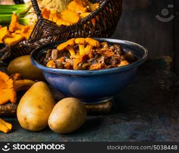 Cooked forest Mushrooms in rustic bowl and potato on dark rustic background, front view. Autumn cooking concept