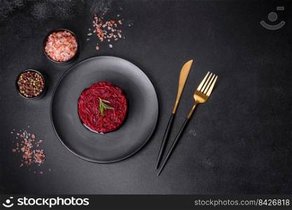 Cooked grated beetroot formed as a cylinder and ready dish on a black plate against a dark concrete background. Cooked grated beetroot formed as a cylinder and ready dish on a black plate