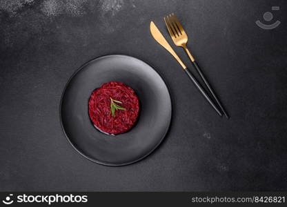 Cooked grated beetroot formed as a cylinder and ready dish on a black plate against a dark concrete background. Cooked grated beetroot formed as a cylinder and ready dish on a black plate