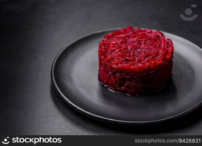 Cooked grated beetroot formed as a cylinder and ready dish on a black plate against a dark concrete background. Cooked grated beetroot formed as a cylinder and ready dish on a black plate