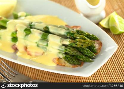 Cooked green asparagus on fried bacon with Hollandaise sauce on top (Selective Focus, Focus on the five asparagus tips in the front). Green Asparagus with Hollandaise Sauce