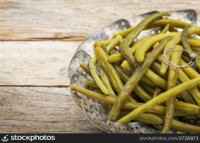 cooked green (French) beans with butter in a metal steamer basket on a rustic wooden table