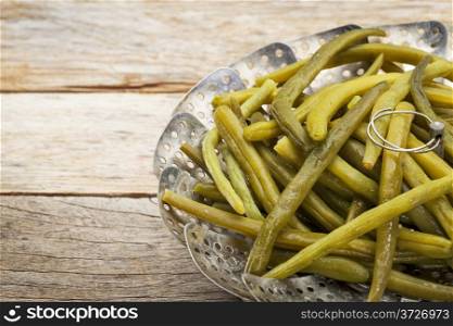 cooked green (French) beans with butter in a metal steamer basket on a rustic wooden table