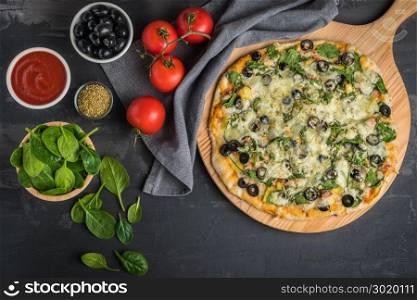 Cooked homemade vegan pizza with spinach, tomatoes, black olives and mozzarella cheese on baking pan over wooden background.