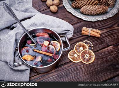 cooked in a steel pan of mulled wine with spices and fruits on a brown wooden background, top view