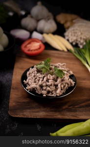 Cooked minced pork with mint leaves on a black plate and tomatoes on a wooden cutting board.