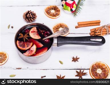 cooked mulled wine in an aluminum pan with a handle on a white wooden background, beside ingredients on a drink recipe