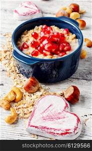 Cooked oat cereal with fruit and nuts on a background of two wooden hearts. Dish of oat flakes