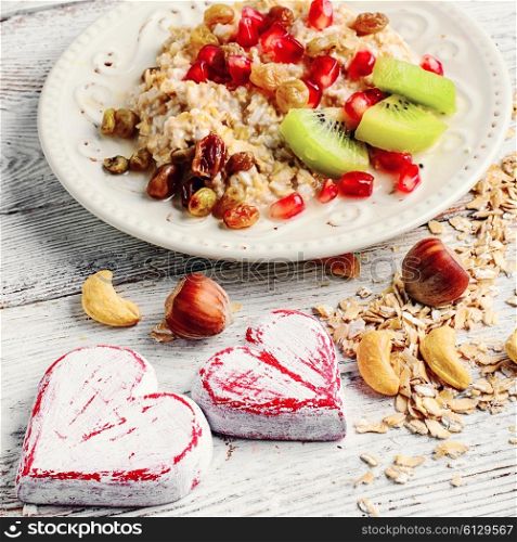 Cooked oat cereal with fruit and nuts on a background of two wooden hearts. Dish of oat flakes