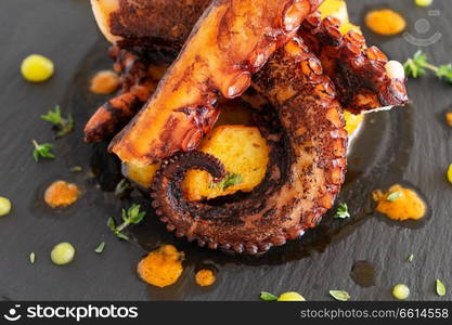 Cooked octopus dish served on black plate. Cooked octopus dish