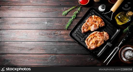 Cooked pork steak in a frying pan grilled with rosemary. On a dark wooden background. High quality photo. Cooked pork steak in a frying pan grilled with rosemary.
