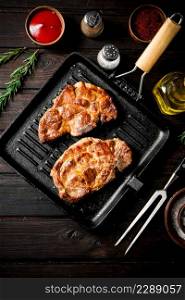 Cooked pork steak in a frying pan grilled with rosemary. On a dark wooden background. High quality photo. Cooked pork steak in a frying pan grilled with rosemary.