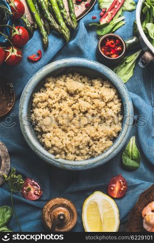 Cooked quinoa in blue bowl with delicious seasonal vegetables and ingredients for salad making on dark background, top view, close up. Superfood , healthy eating or vegetarian food concept.