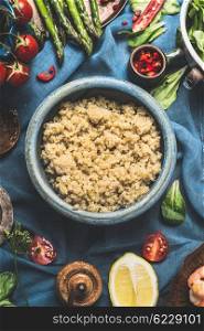 Cooked quinoa in blue bowl with delicious seasonal vegetables and ingredients for salad making on dark background, top view, close up. Superfood , healthy eating or vegetarian food concept.