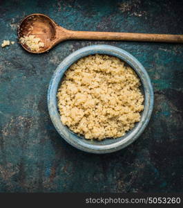 Cooked quinoa seeds in rustic bowl with wooden cooking spoon on dark vintage background, top view, close up