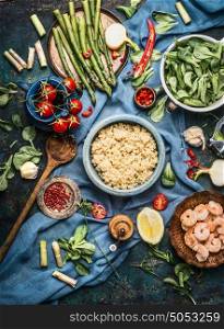 Cooked quinoa with green asparagus and other vegetables ingredients for healthy cooking on dark rustic kitchen table background with cooking spoon and bowls, top view. Clean organic food concept