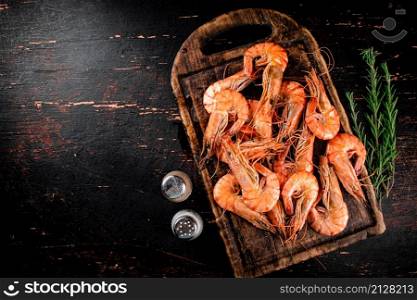 Cooked shrimp on a cutting board with spices and rosemary. Against a dark background. High quality photo. Cooked shrimp on a cutting board with spices and rosemary.