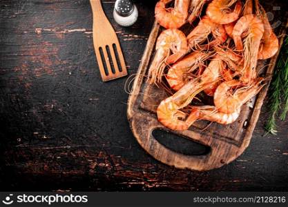 Cooked shrimp on a cutting board with spices and rosemary. Against a dark background. High quality photo. Cooked shrimp on a cutting board with spices and rosemary.