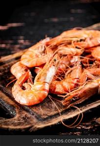 Cooked shrimp on a wooden cutting board. Against a dark background. High quality photo. Cooked shrimp on a wooden cutting board.