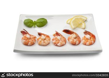 Cooked shrimps with lemon and basil leaves on a dish on white background