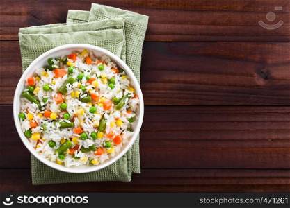 Cooked white rice mixed with colorful vegetables (onion, carrot, green peas, corn, green beans) in white bowl, photographed overhead with copy space on the right side. Rice with Vegetables