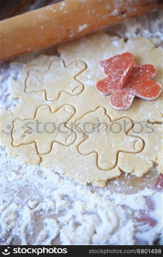 Cookie dough with teddy bear shapes and rolling pin on floured surface