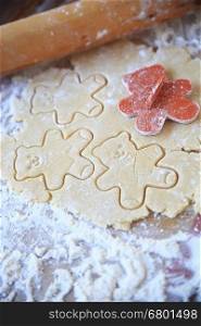 Cookie dough with teddy bear shapes and rolling pin on floured surface