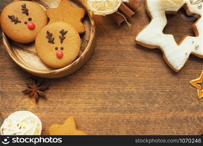 Cookies with a muzzle of a deer and in the shape of a star, a garland, cinnamon and star anise star on a brown wooden background. Space for an inscription.