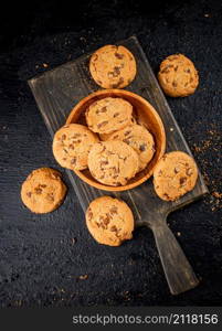 Cookies with milk chocolate on a cutting board. On a black background. High quality photo. Cookies with milk chocolate on a cutting board.