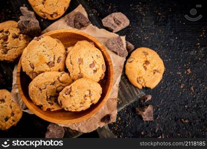Cookies with pieces of milk chocolate on a cutting board. On a black background. High quality photo. Cookies with pieces of milk chocolate on a cutting board.