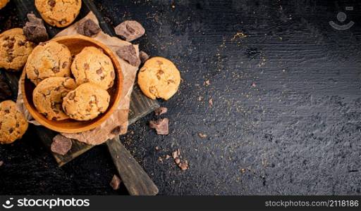 Cookies with pieces of milk chocolate on a cutting board. On a black background. High quality photo. Cookies with pieces of milk chocolate on a cutting board.