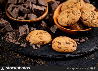 Cookies with pieces of milk chocolate on a stone board. On a black background. High quality photo. Cookies with pieces of milk chocolate on a stone board.