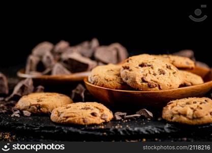 Cookies with pieces of milk chocolate on a stone board. On a black background. High quality photo. Cookies with pieces of milk chocolate on a stone board.