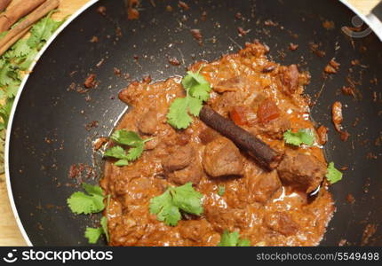 Cooking a balti lamb and yoghurt curry in a wok, high angle view.