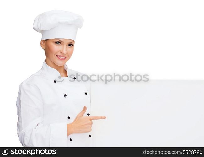 cooking, advertisement and food concept - smiling female chef, cook or baker pointing finger to white blank board