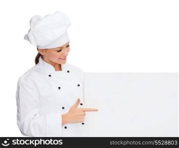 cooking, advertisement and food concept - smiling female chef, cook or baker pointing finger to white blank board