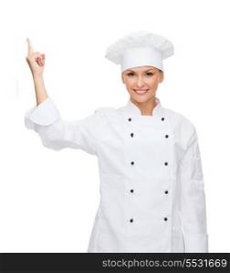 cooking, advertisement and food concept - smiling female chef, cook or baker pointing finger up to something