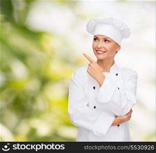 cooking, advertisement and food concept - smiling female chef, cook or baker pointing finger to something