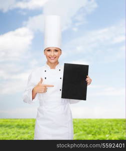 cooking, advertisement and food concept - smiling female chef pointing finger to blank black paper