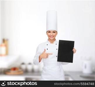 cooking, advertisement and food concept - smiling female chef pointing finger to blank black paper