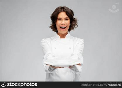 cooking, advertisement and people concept - happy smiling female chef holding empty plate over grey background. smiling female chef holding empty plate